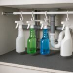 Tension rod hanging spray bottles under sink with waterproof mat